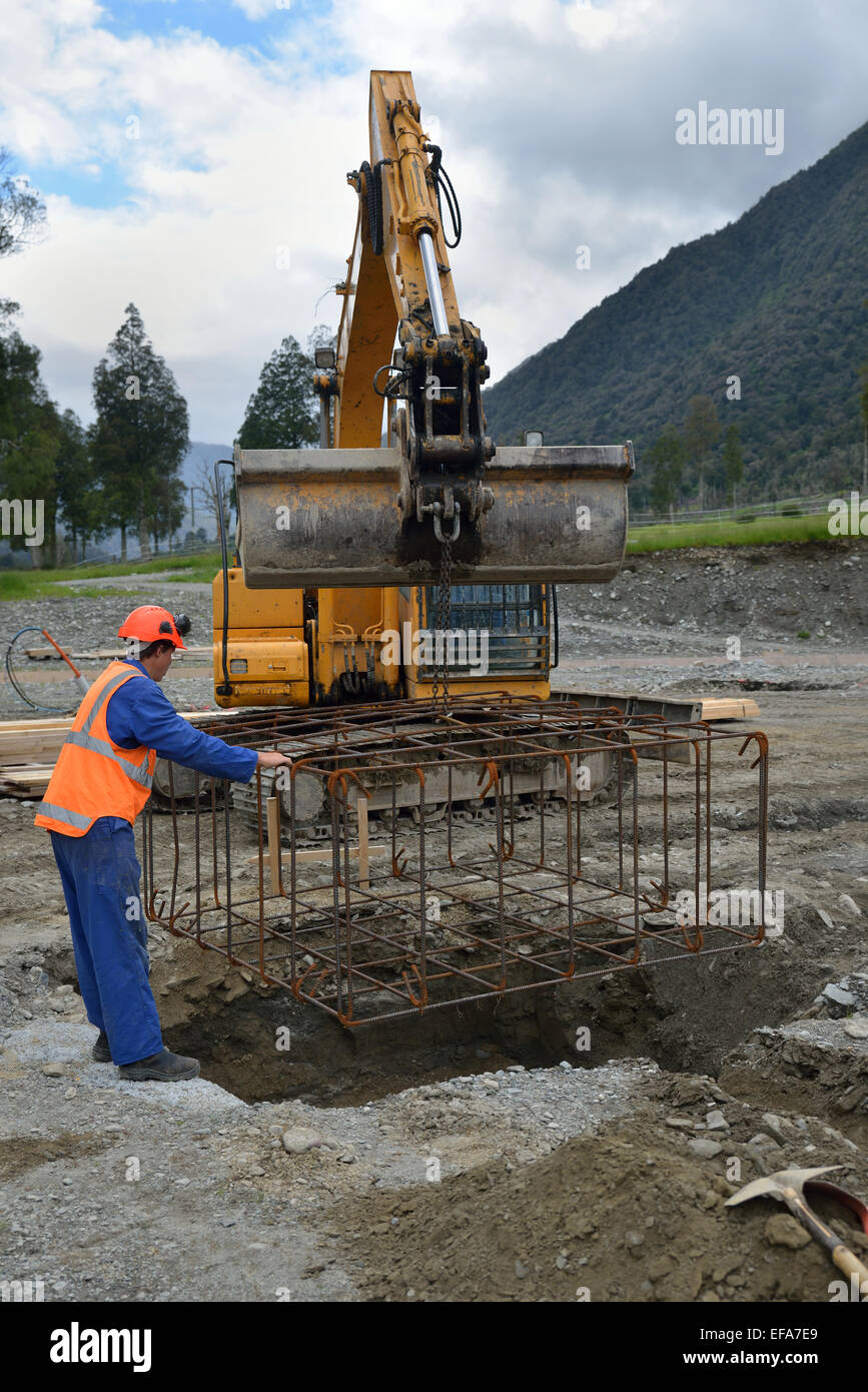A builder directs a cage of reinforcing rods into the foundation for a portal a large building Stock Photo