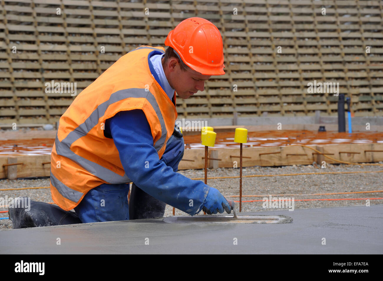 A builder floats off wet concrete with a steel trowel for the foundations of a large building Stock Photo