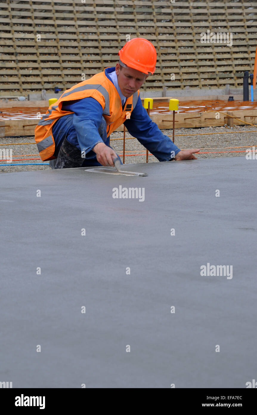 A builder floats off wet concrete with a steel trowel for the foundations of a large building Stock Photo