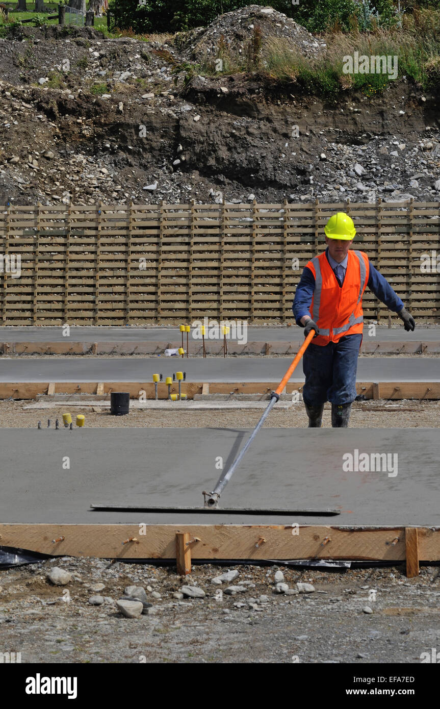 A builder uses a long handled trowel to float off a wet concrete slab for a large building Stock Photo