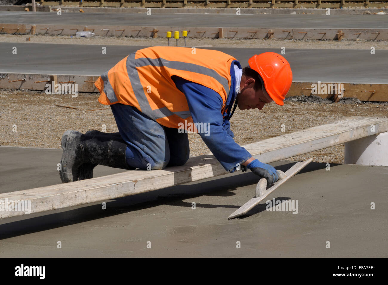 A builder uses a wooden trowel to float off a wet concrete slab for a large building Stock Photo