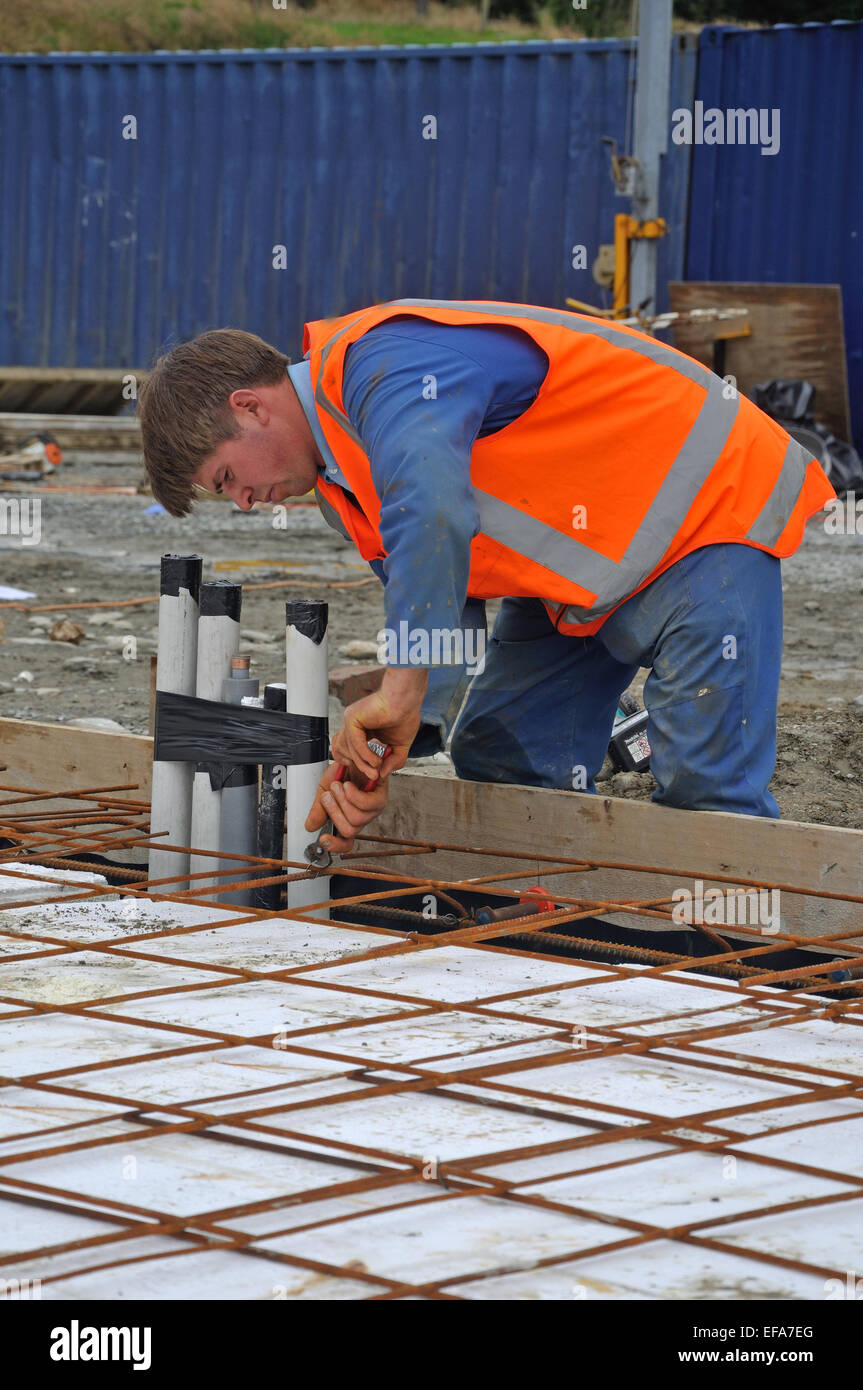 A builder ties off the reinforcing before concrete is poured into the foundations of a large building Stock Photo
