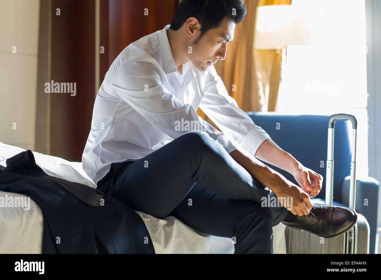 Young businessman tying shoes in hotel room Stock Photo Alamy