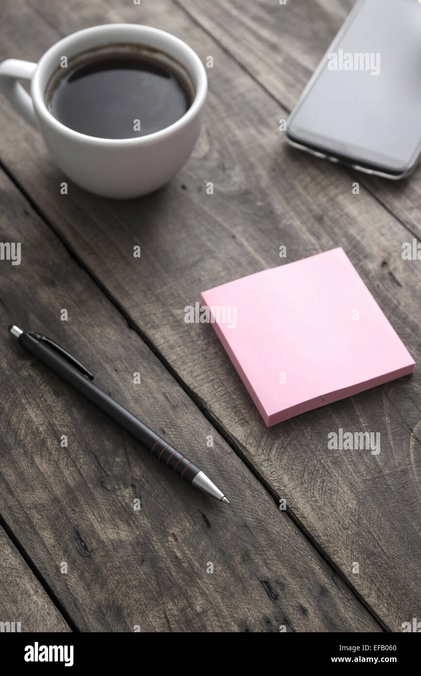 Smart phone  with sticky note paper and cup of coffee on old wooden desk. Stock Photo