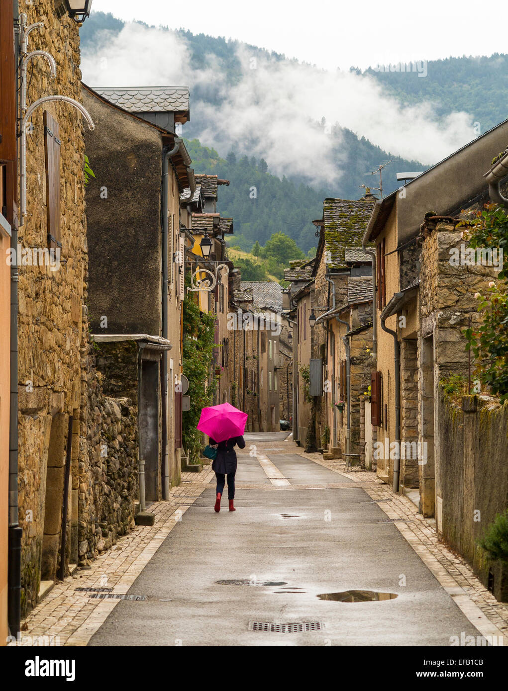 Woman with umbrella walking in the medieval French village of Quezac, the Lozère Stock Photo