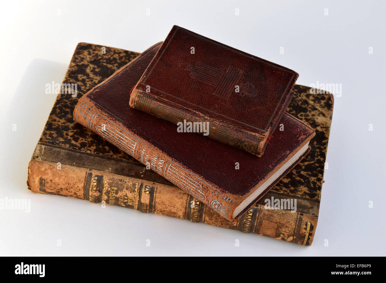 Old three books with red and brown hard cover and golden letters leaning over a white background Stock Photo
