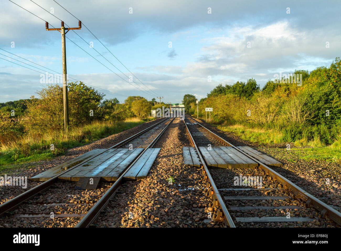 Straight railway track running into the distance with wooden planks forming an unmanned and unprotected level crossing, Nottinghamshire, England, UK Stock Photo