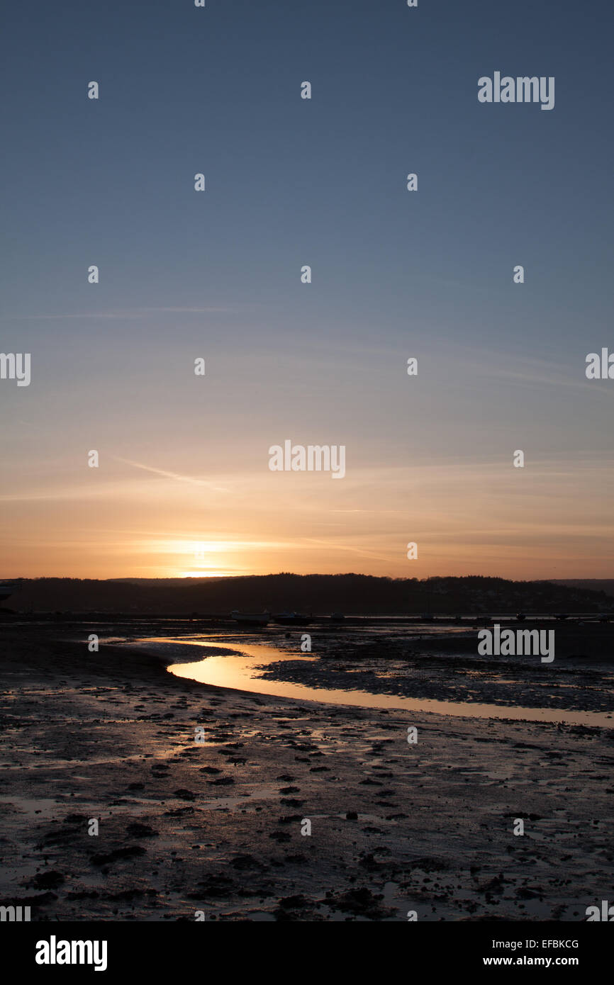 muddy estuary at sunset and low tide. Reflection of sun. Blue sky Stock Photo