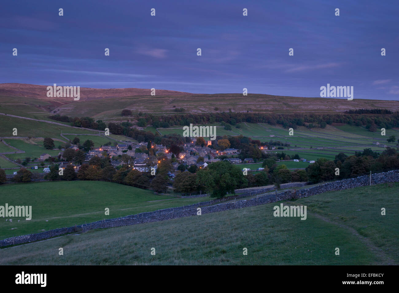 Kettlewell village, nestling in scenic valley below upland moors & hills, street lights lit at nightfall - Wharfedale, Yorkshire Dales, England, UK. Stock Photo