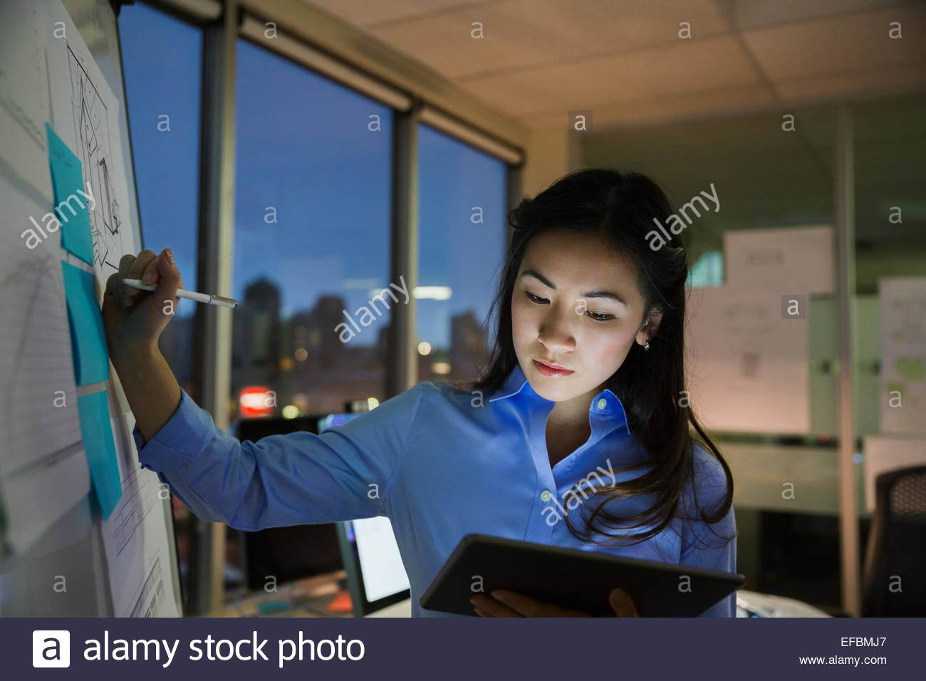 Businesswoman at whiteboard working late in conference room Stock Photo