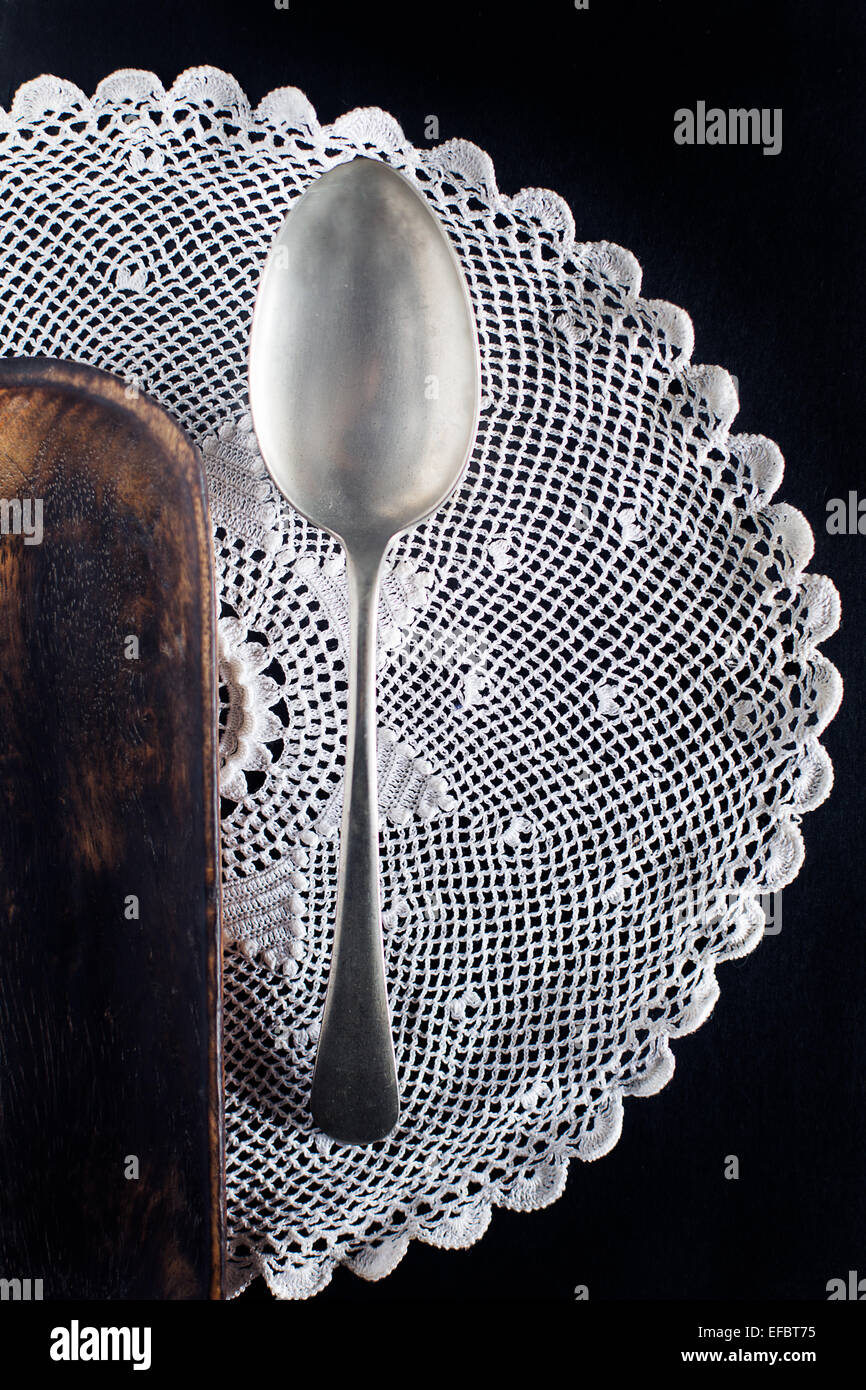 Silver Spoon on lace Doily on black, wood platter at side Stock Photo