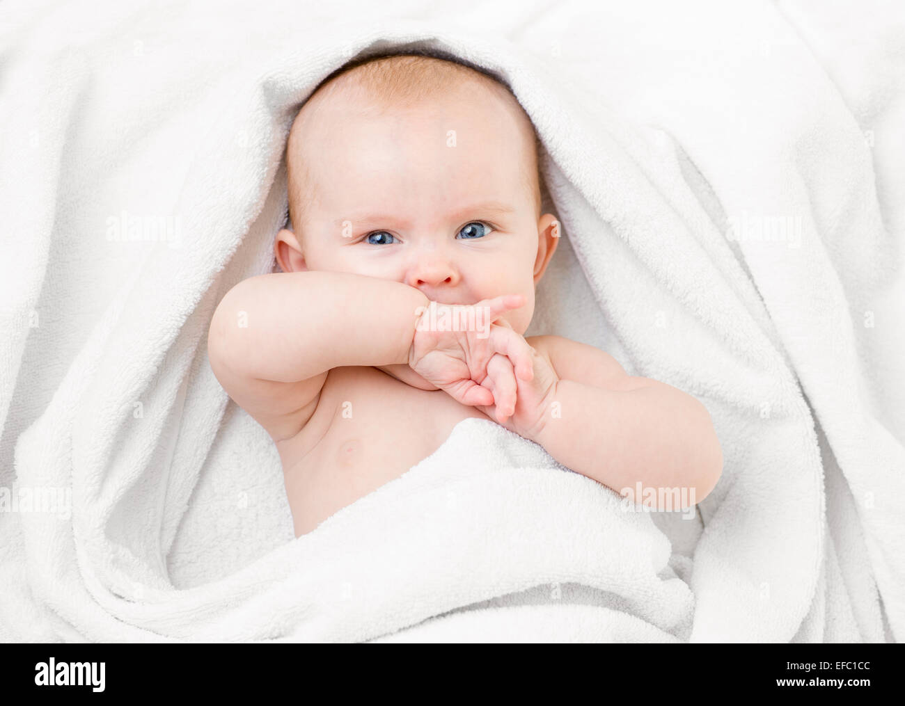 Cute baby lying on white towel and sucking own hand Stock Photo