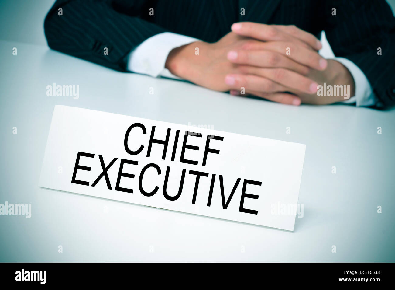 a man in suit sitting at a desk with a signboard in front of him with the text chief executive written in it Stock Photo