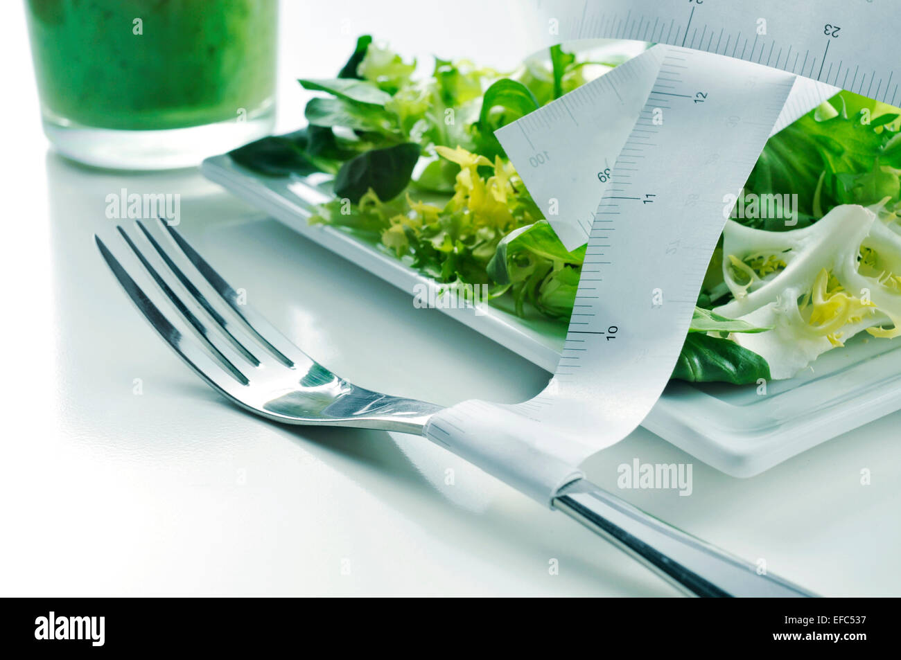 closeup of a plate with a green salad and a measuring tape and a green smoothie, depicting the concept of dieting or to stay fit Stock Photo