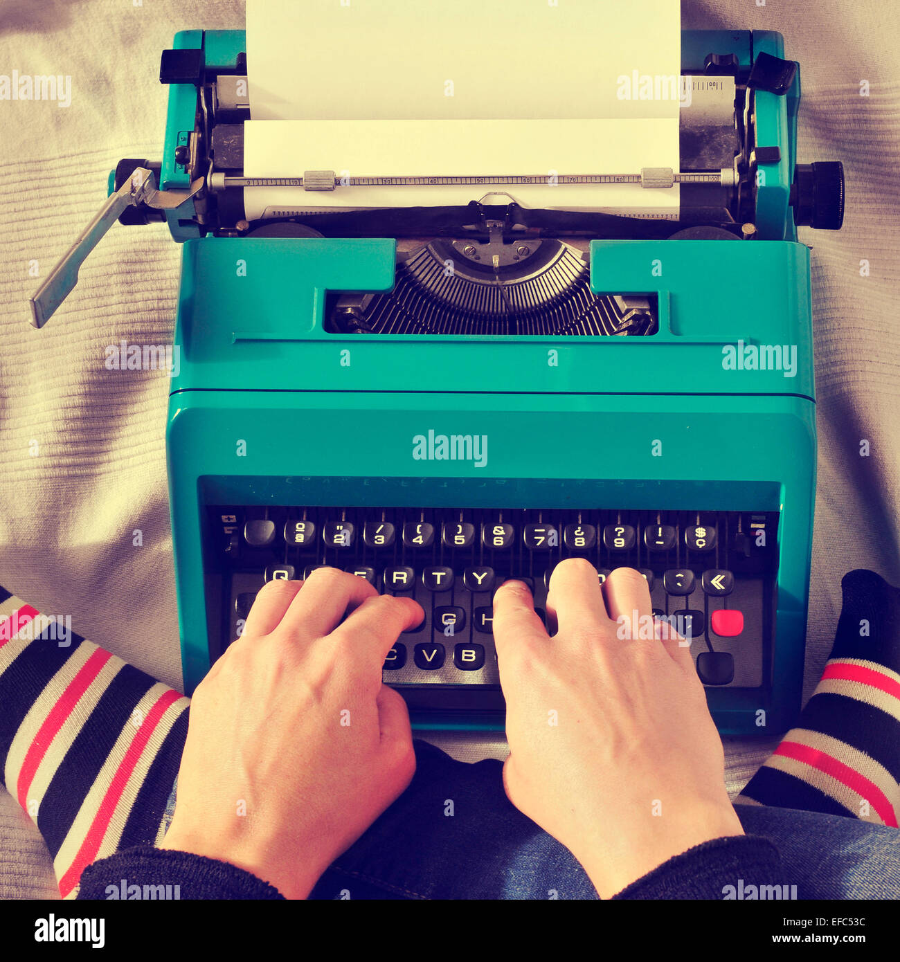 a young man typing in an old typewriter on the bed, with a retro effect Stock Photo