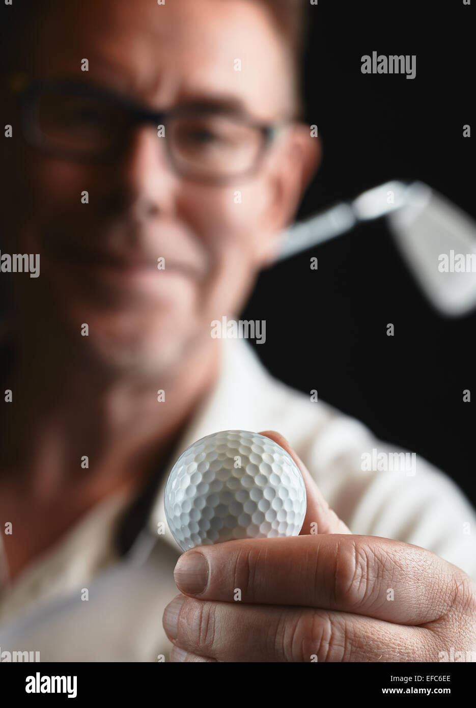 Close up, mature man golfer wearing a white shirt and he holds a golf ball on hand, iron golf club on his shoulder - focus on ba Stock Photo