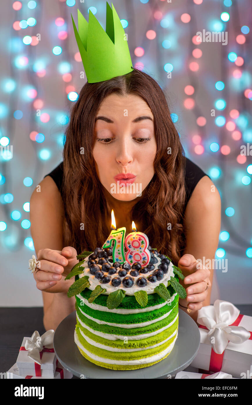 Eighteen girl with happy birthday cake blowing up candles on festive light background Stock Photo