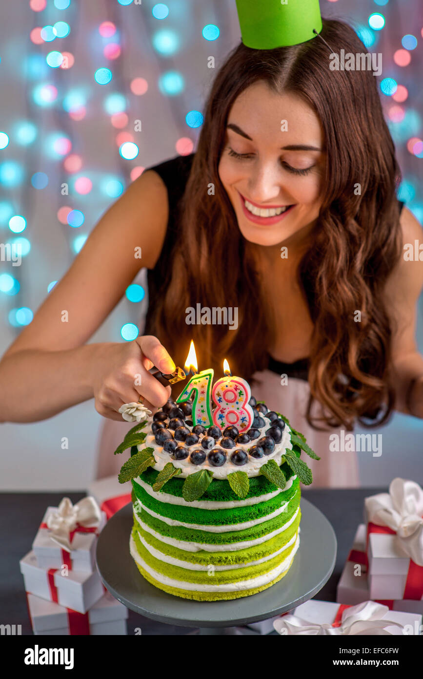 Eighteen girl with happy birthday cake lighting candles on festive light background Stock Photo
