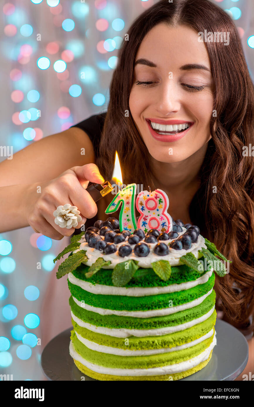 Eighteen girl with happy birthday cake lighting candles on festive light background Stock Photo