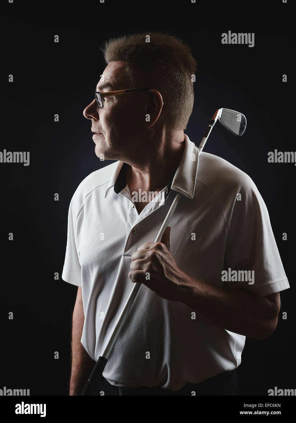 Mature man golfer wearing a white shirt and he holds a iron golf club on his shoulder and he looking away - studio shot, black b Stock Photo