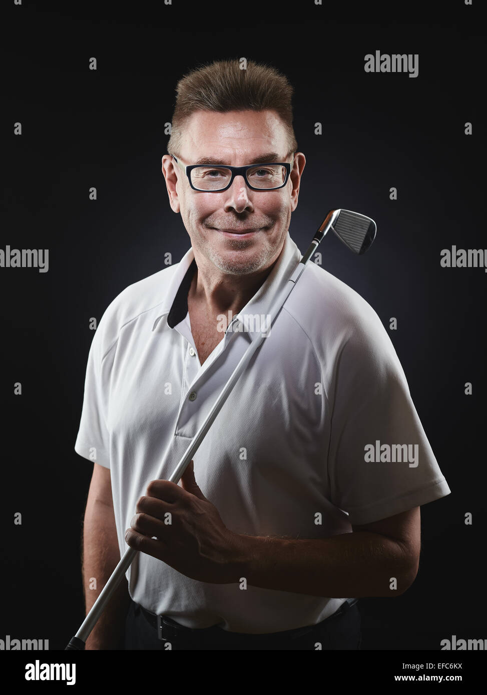 Mature man golfer wearing a white shirt and he holds a iron golf club on his shoulder and he looking at camera - studio shot, bl Stock Photo