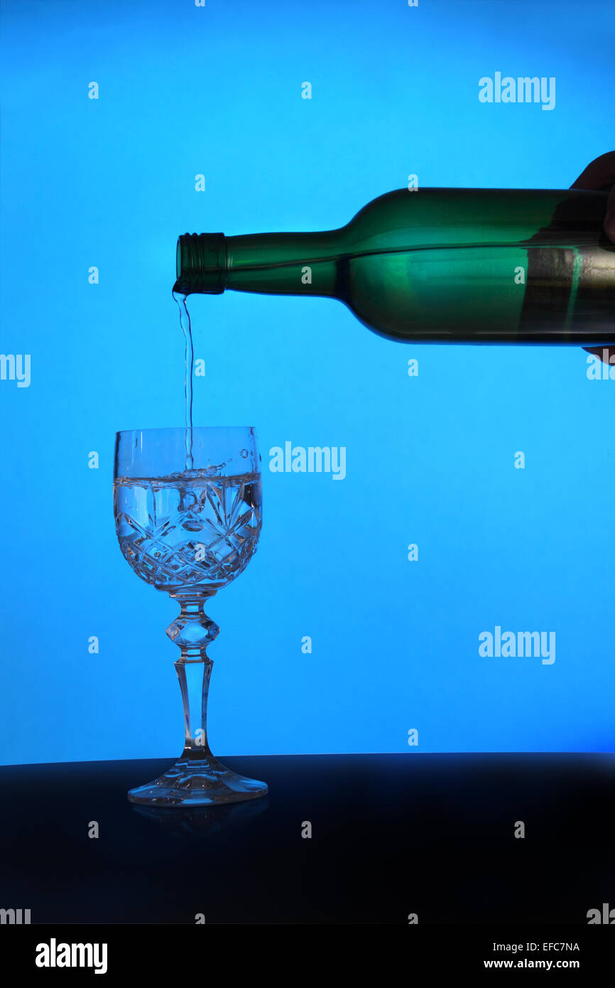 Background image showing a moody, back lit bottle of wine being poured into a diamond cut glass. Stock Photo