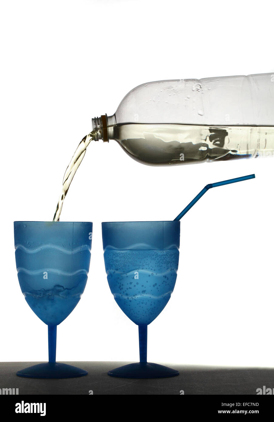 Shop brought clear lemonade being poured from a plastic bottle into a blue plastic beaker with a second beaker containing lemonade and a blue straw Stock Photo