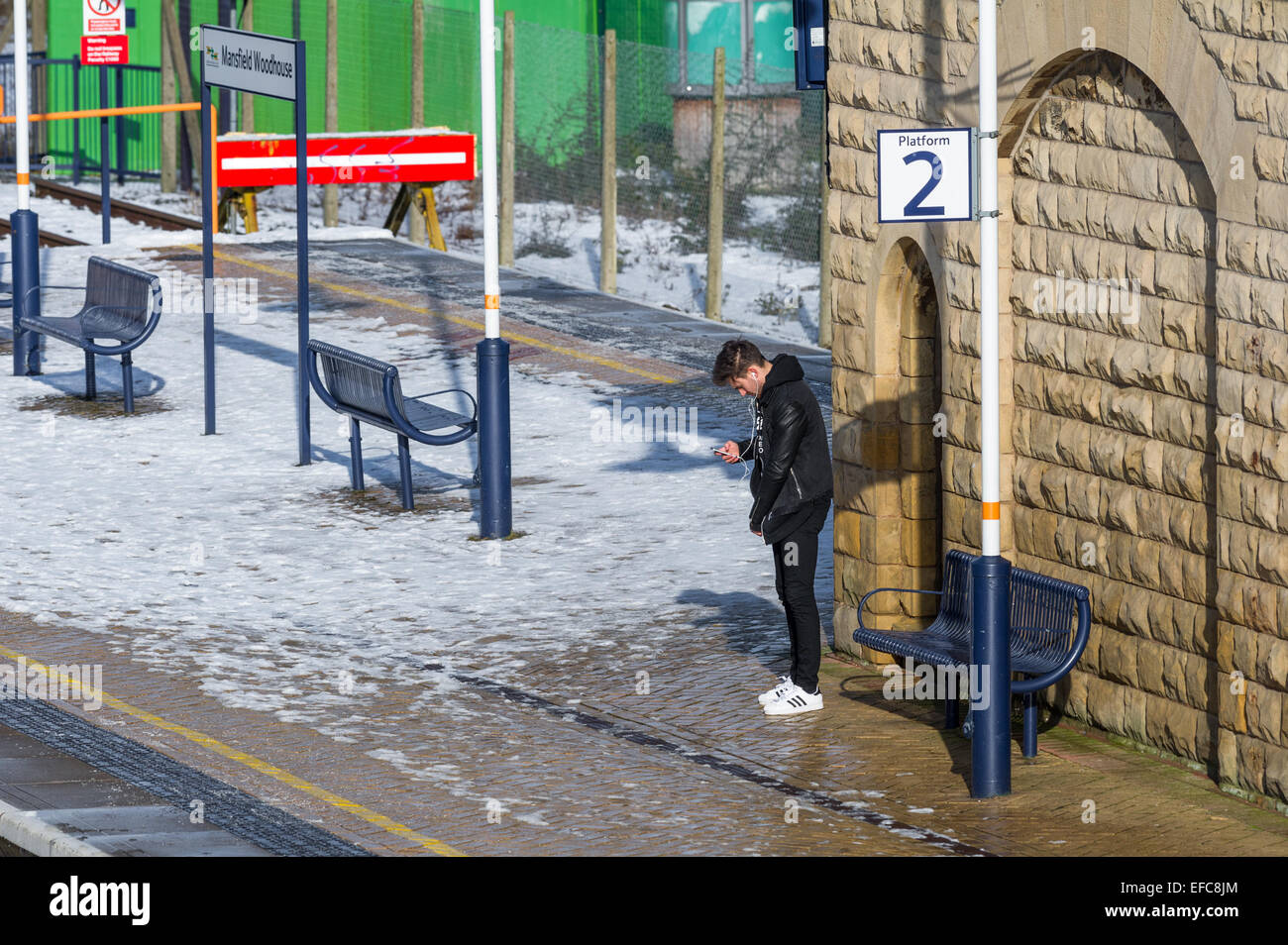 Male waiting for a train on platform two whilst using his mobile phone. Stock Photo