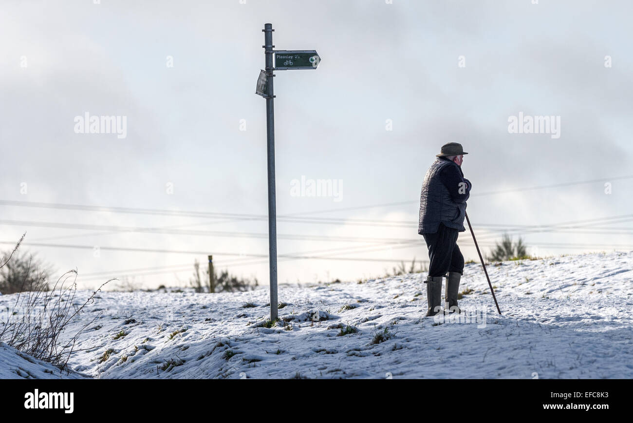 Elderly man resting on his walking stick and wearing winter clothing and wellington boots with snow on the ground. Stock Photo
