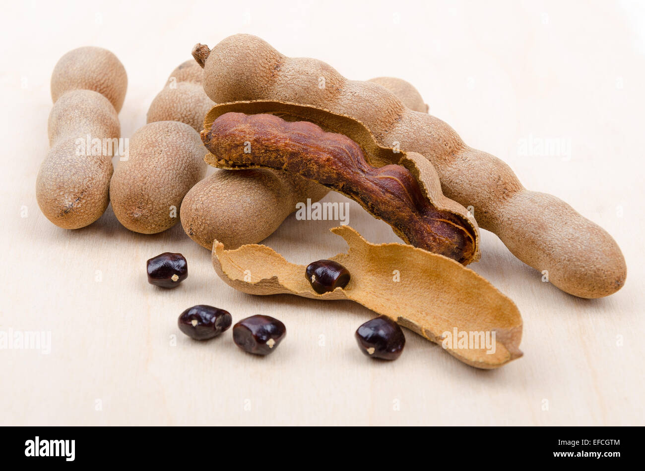 Dried tamarind fruits with seeds on wood. One open pod with pulp inside its shell. Tamarindus indica. Stock Photo