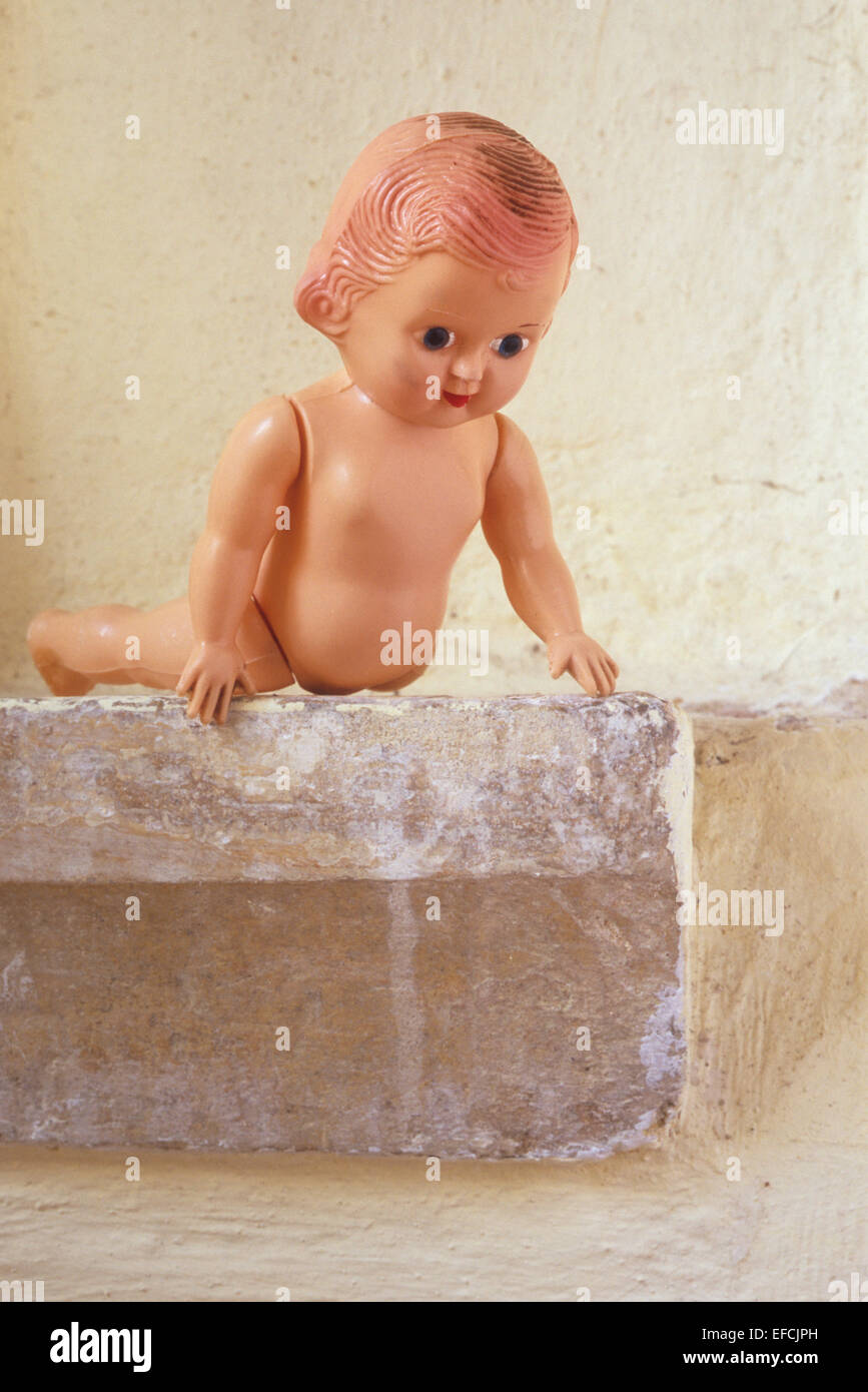 Vintage baby doll leaning forward over stone ledge as if admiring view or considering jumping Stock Photo