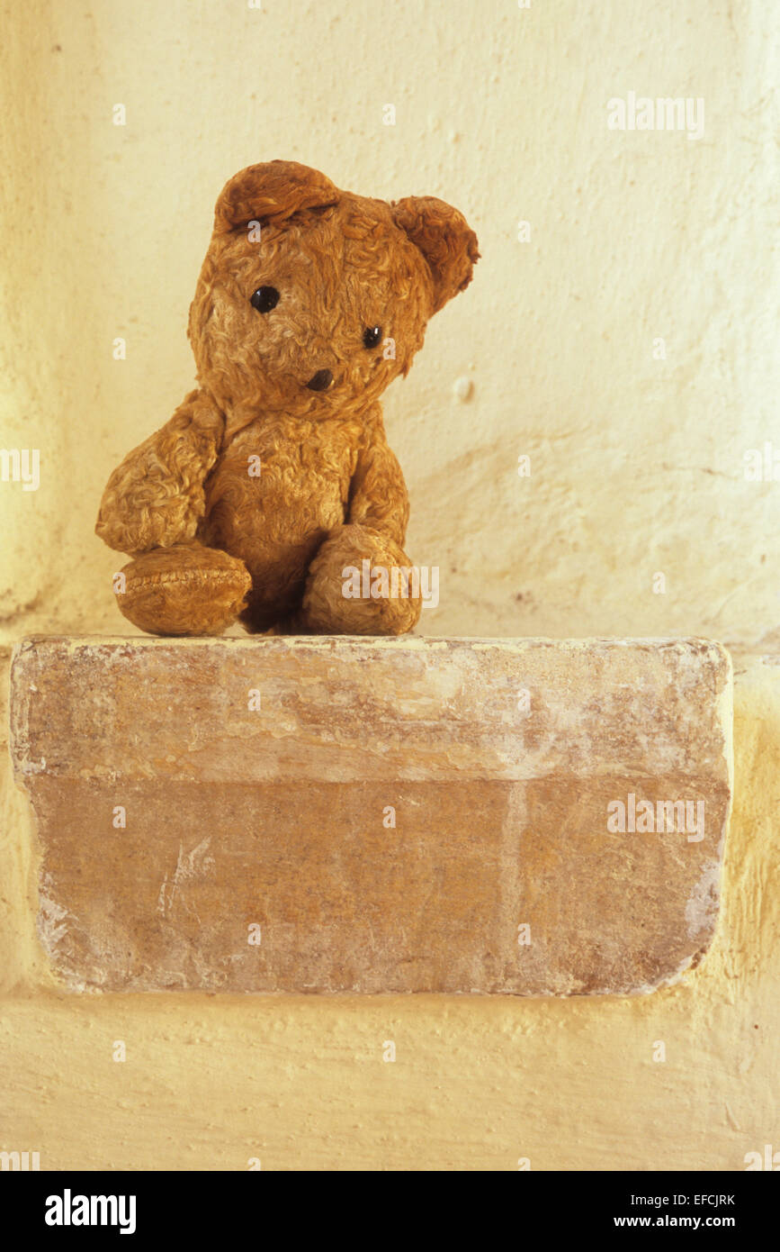 Vintage teddy bear sitting on stone ledge looking sad as if trapped or forgotten Stock Photo