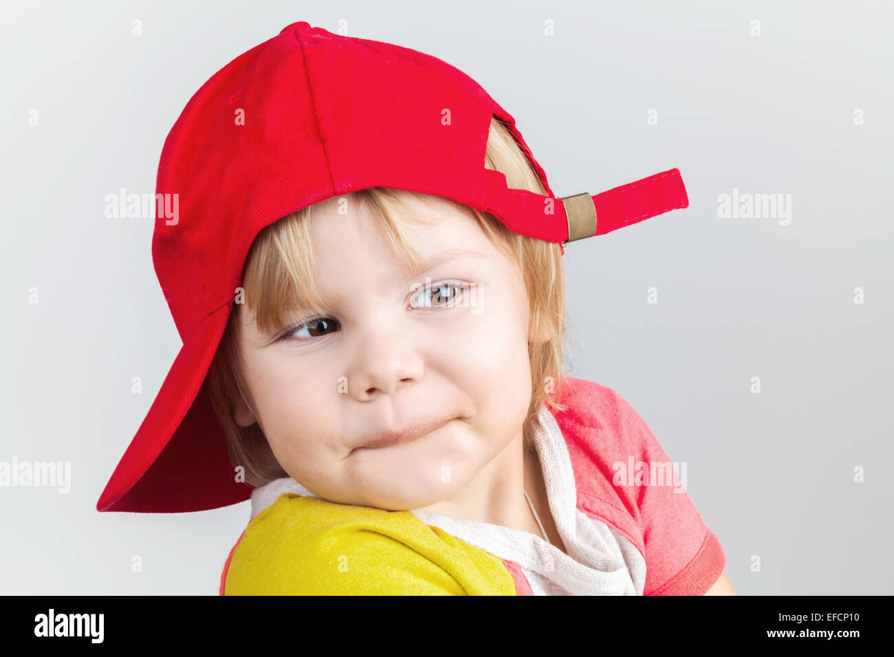 Studio portrait of funny smiling baby girl in red baseball cap over gray wall background Stock Photo