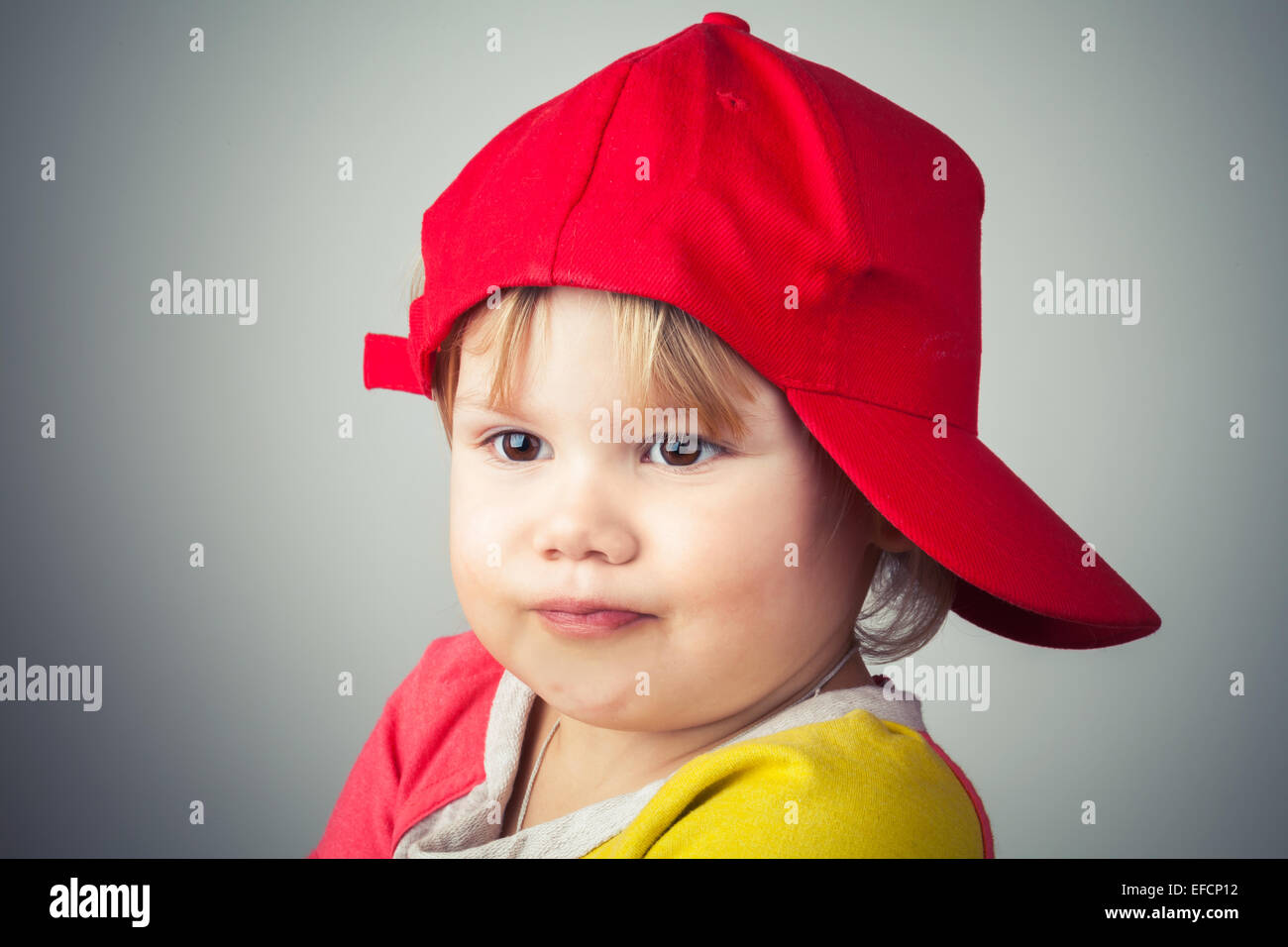 Studio portrait of funny baby girl in red baseball cap over gray wall background. Vintage style, photo filter effect Stock Photo