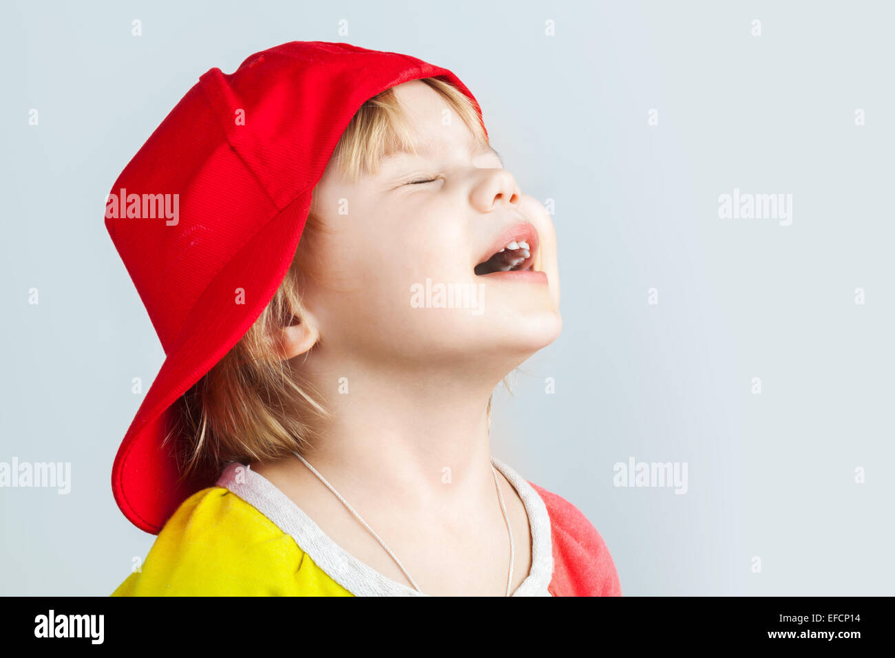 Studio portrait of happy baby girl in red baseball cap over gray wall background Stock Photo