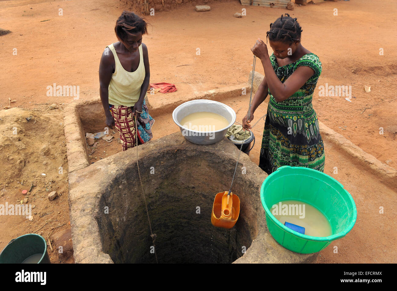 Two women draw dirty water from a nearly dry well in an arid region of Ghana. Stock Photo