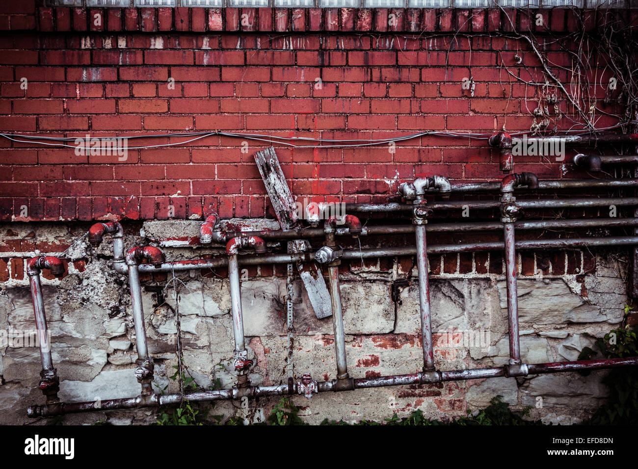 A maze of connected pipes and wires are attached to a red brick wall on the exterior of a building. Stock Photo