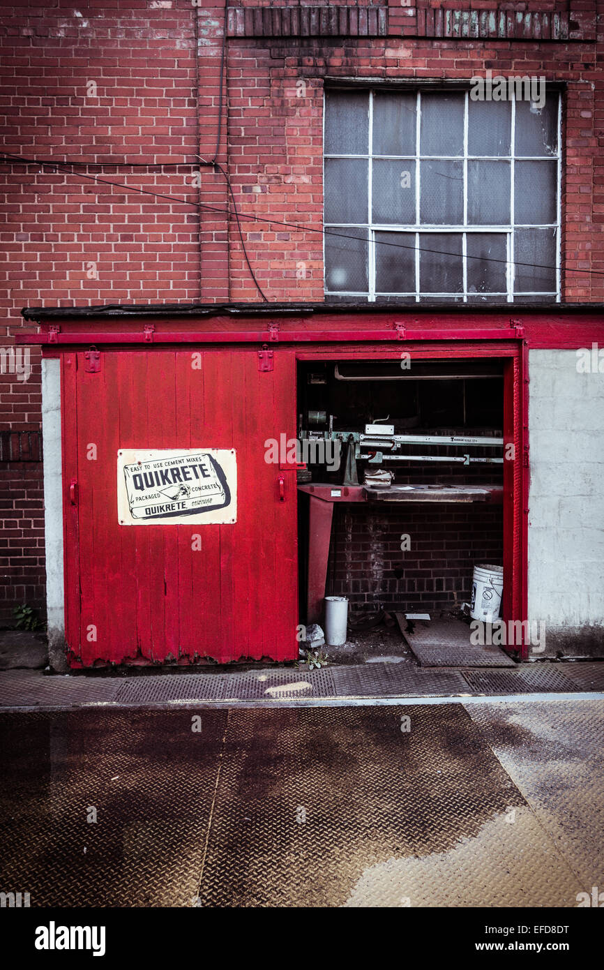 An industrial scale sits in a small red building next to a red brick building. Stock Photo