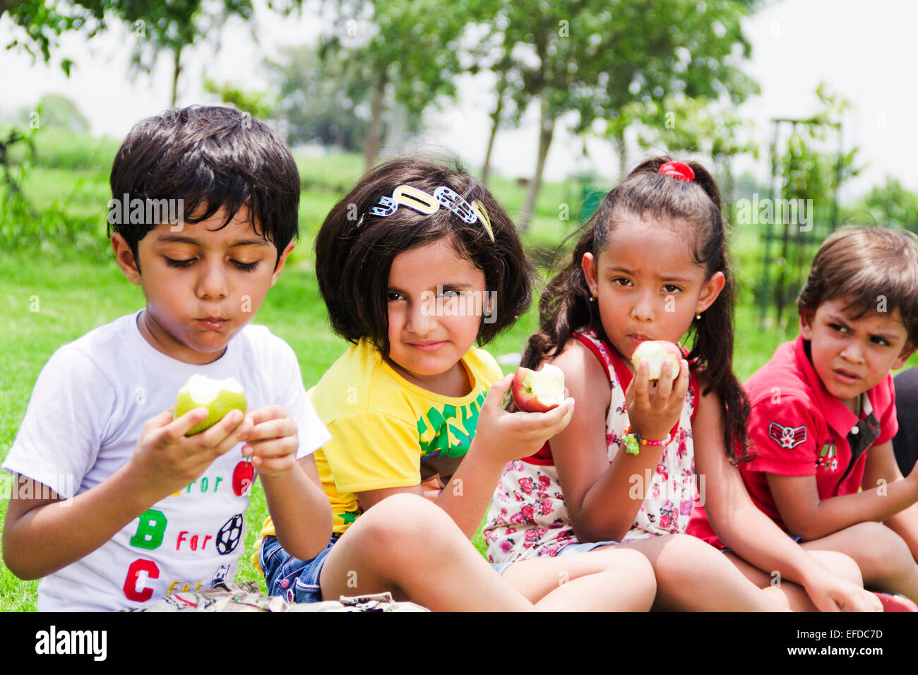 4 indian children friends Picnic Park Eating Apple Stock Photo