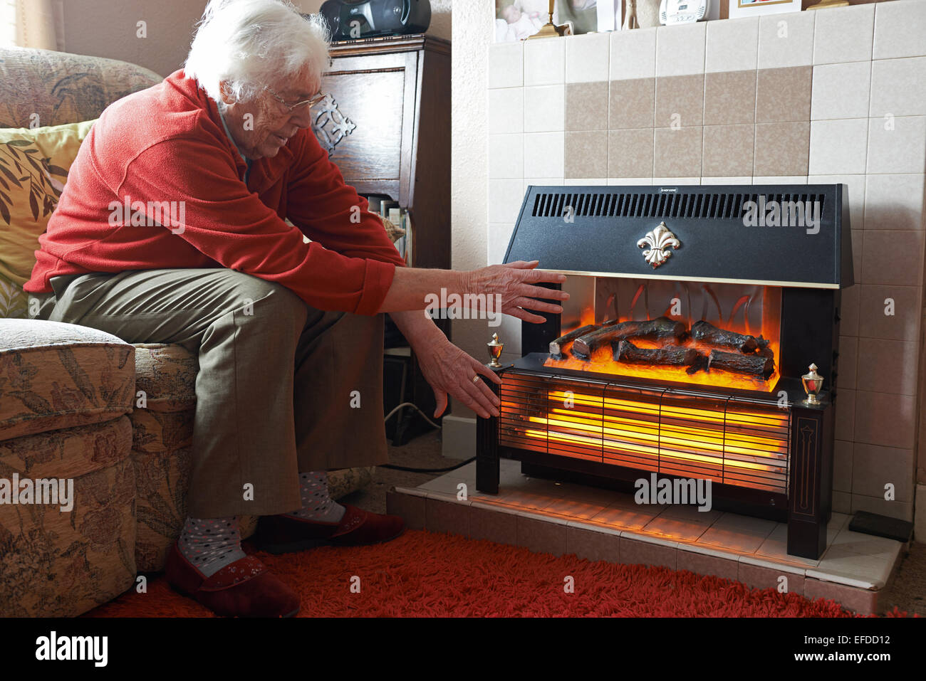 Old aged pensioner trying to keep warm beside an electric heater Stock Photo