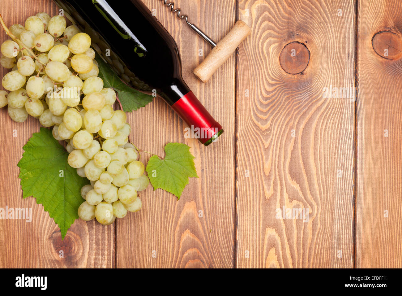 Red wine bottle and bunch of white grapes on wooden table background ...