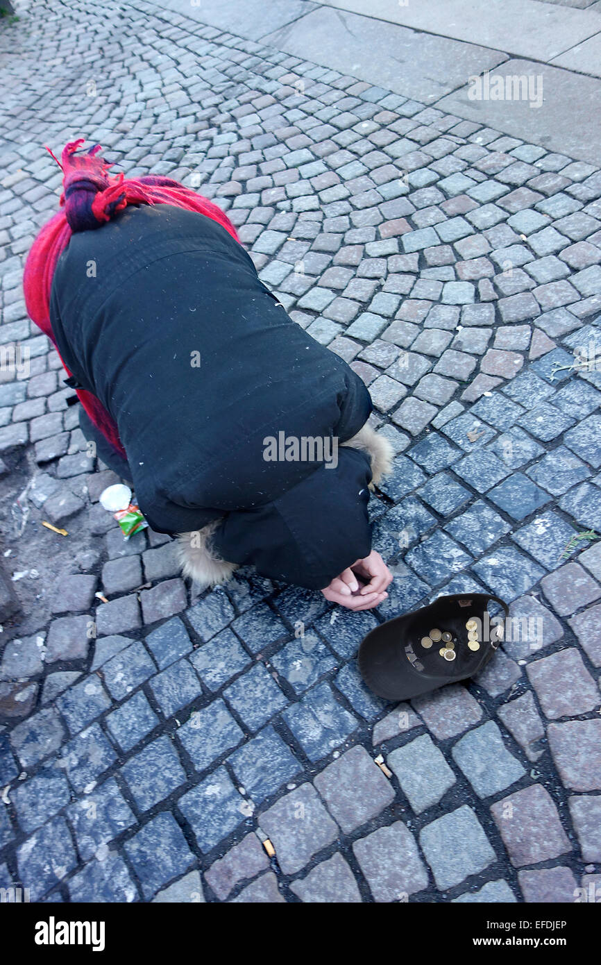 A beggar bows kneeling on a cobbled pavement begging for alms Stock Photo