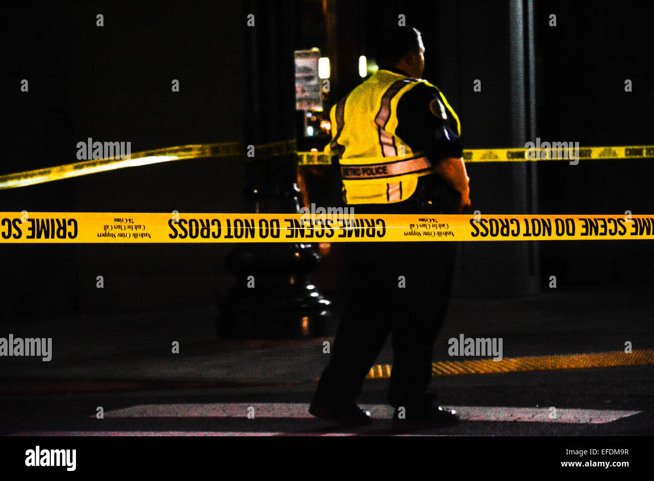 Yellow crime tape wraps around a street intersection at night with a