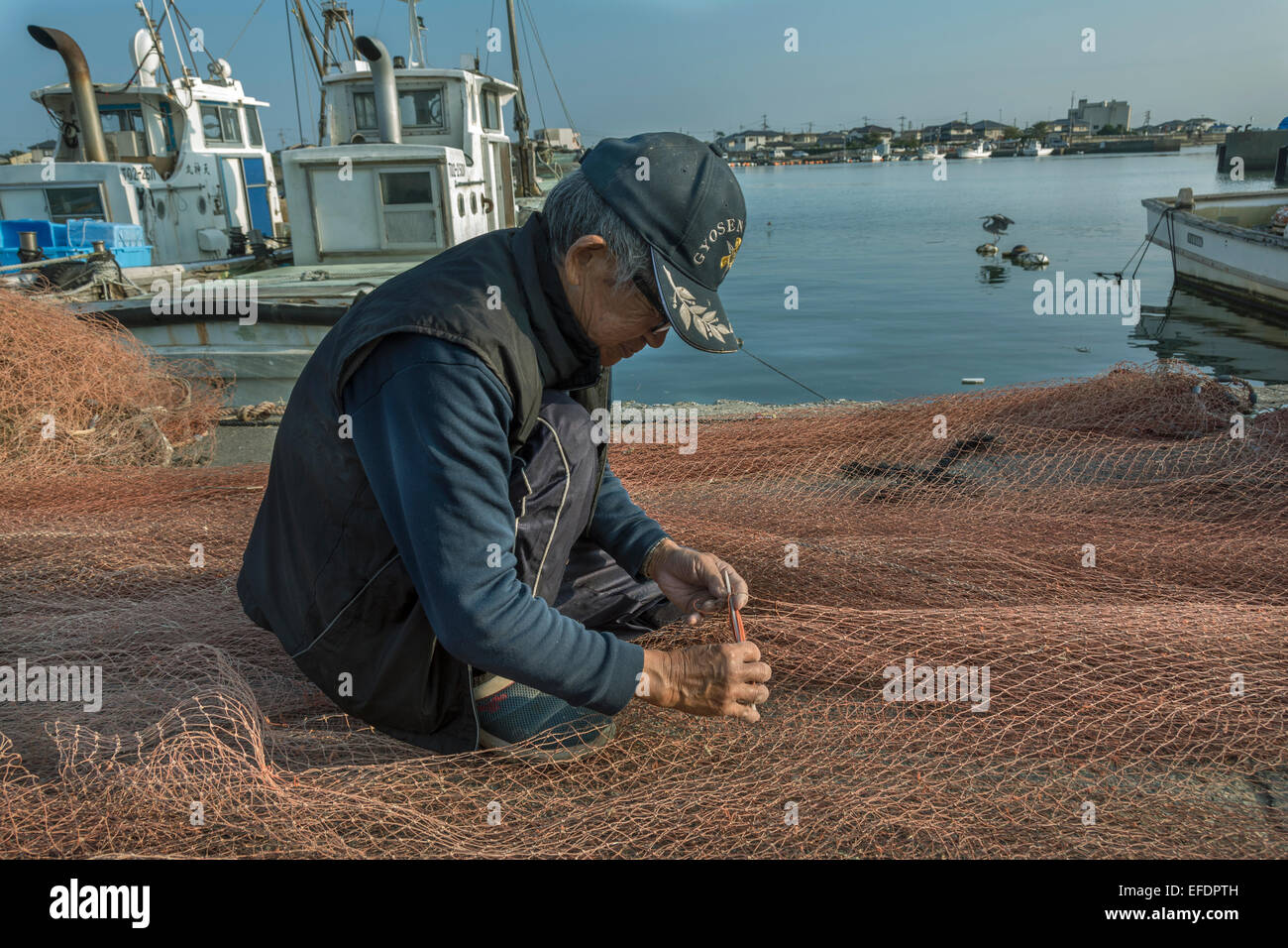 Old man repairing fishing nets by hand, Naruto Harbor, Shikoku Island, Japan Stock Photo