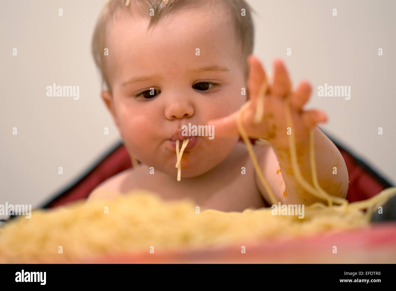 A ten month old baby girl eating pasta. Photo Tim Clayton Stock Photo