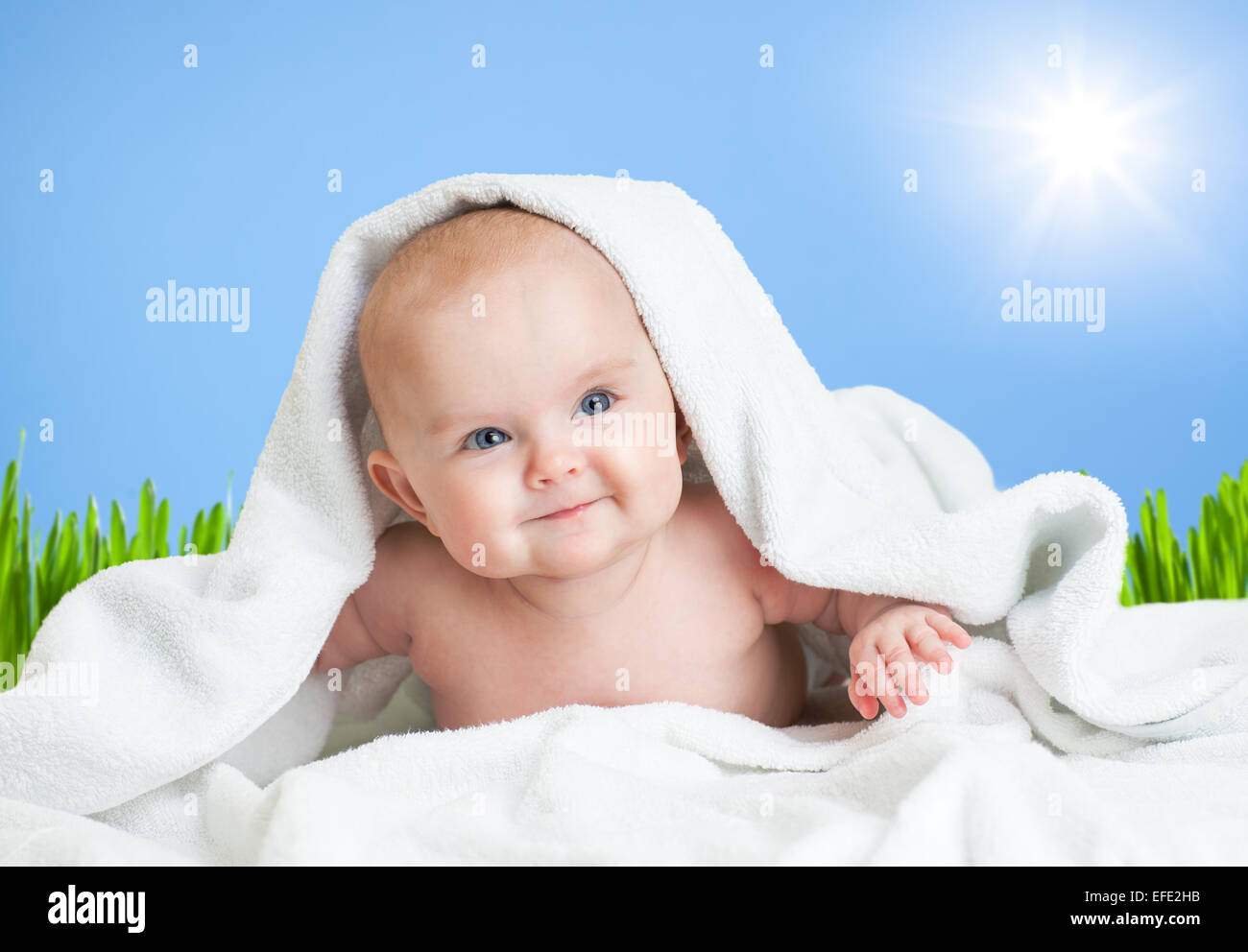 Cute smiling baby in towel on fresh air under sky and sun Stock Photo
