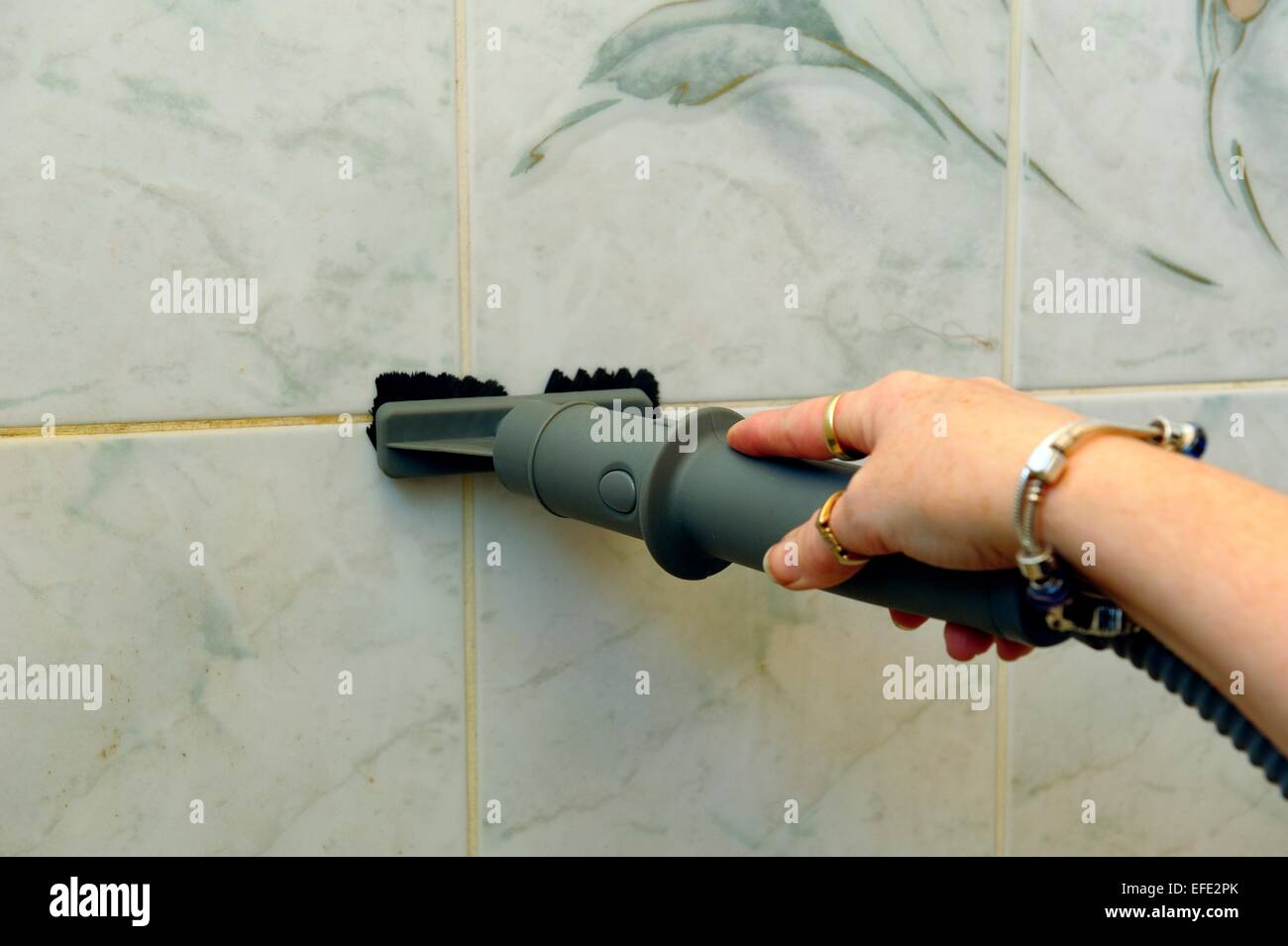 A woman using a steam cleaner on bathroom tiles Stock Photo