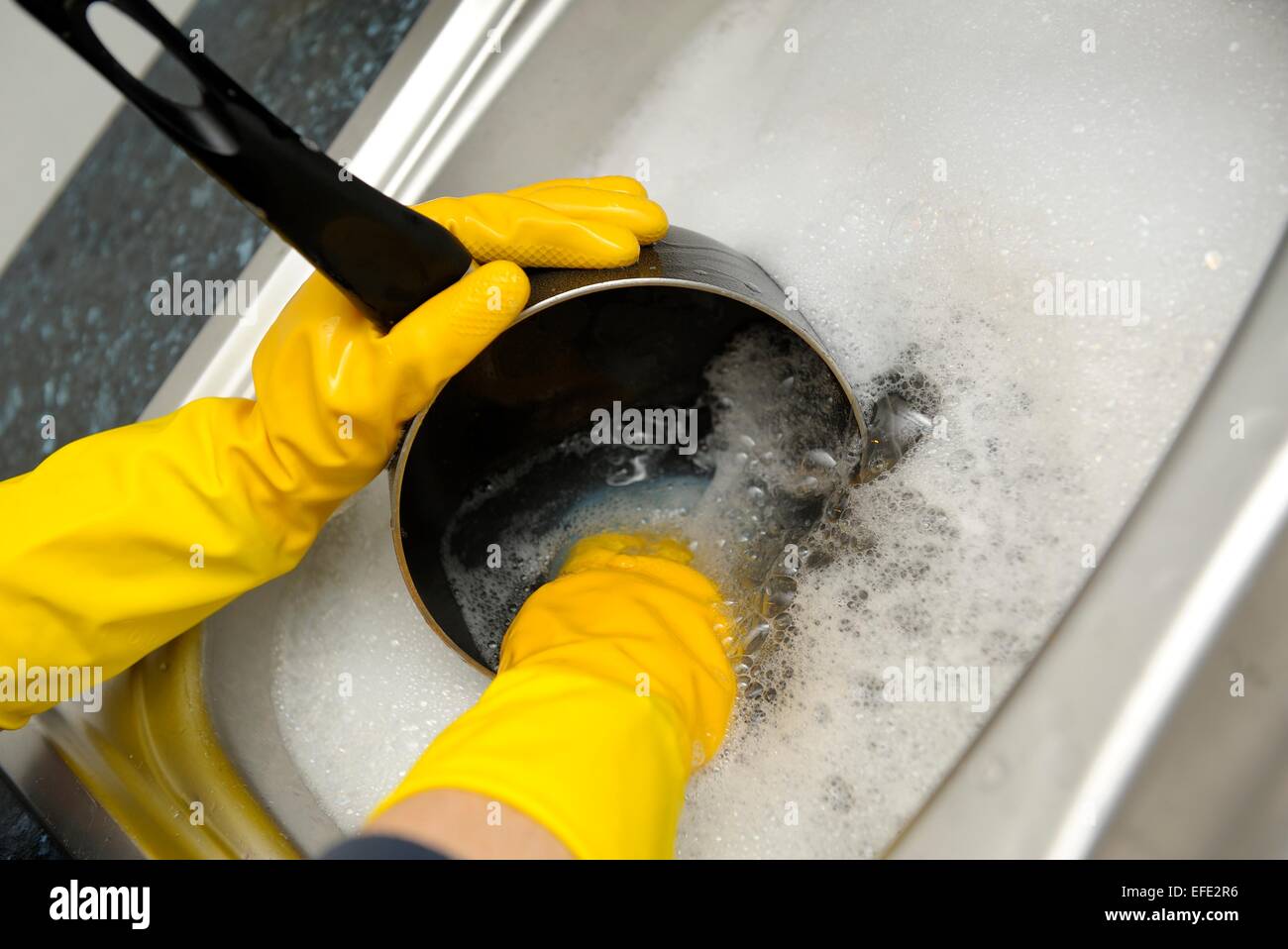 A woman washing pots wearing yellow rubber gloves Stock Photo