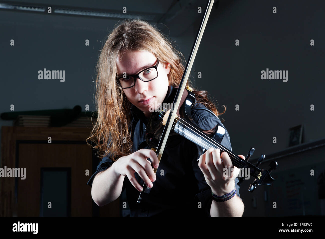young man with long hair and glasses plays electric violin with harsh light  Stock Photo - Alamy
