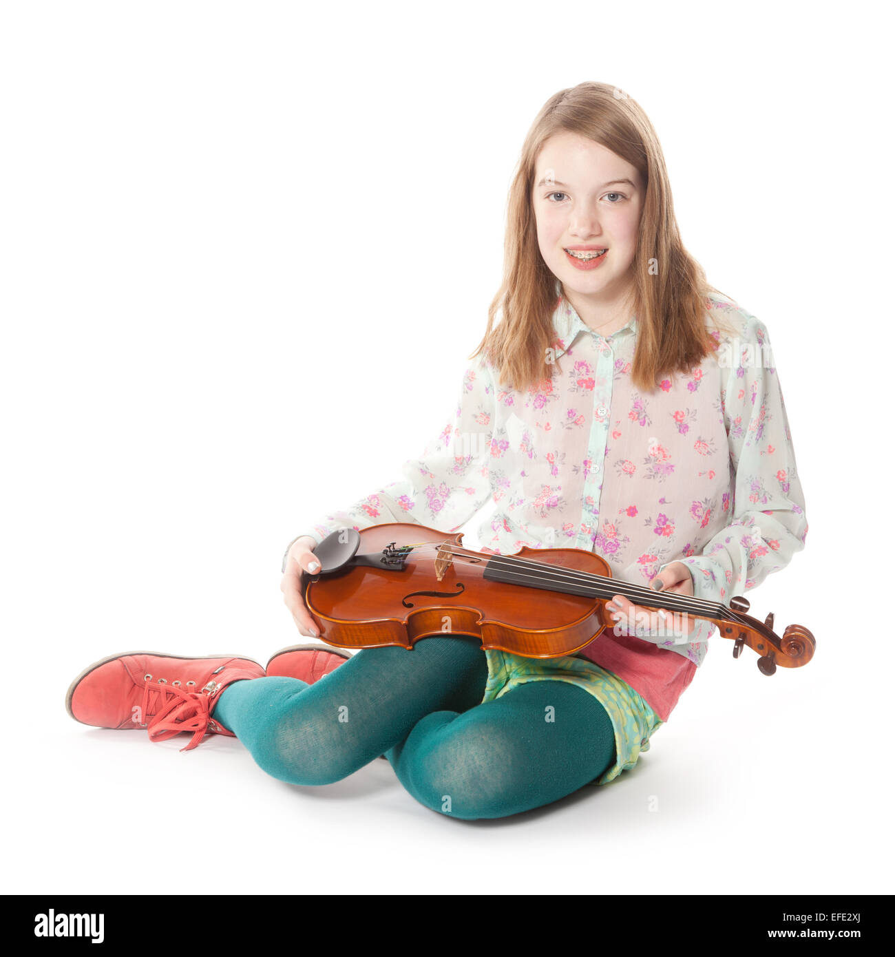 young girl sits in studio against white background and holds violin ...